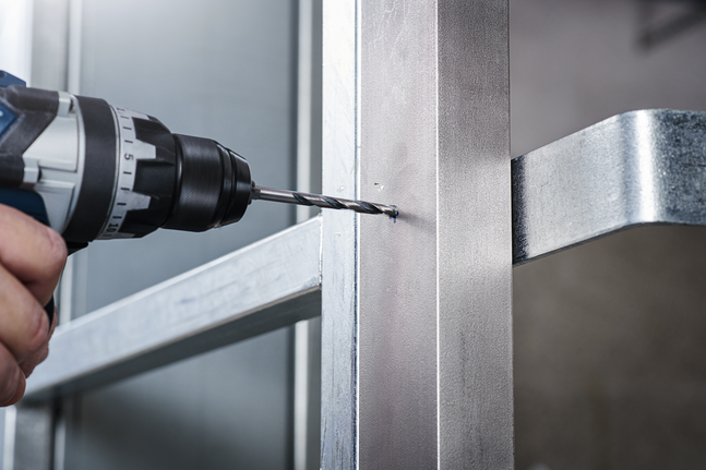 يقوم الشخص بحفر ثقب في إطار معدني باستخدام مثقاب لاسلكي.