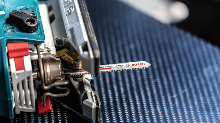 منشار كهربائي بشفرة معدنية مثبتة على سطح أزرق محبب.