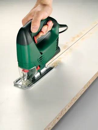 A jigsaw is cutting a straight line through a sheet of wood.