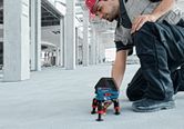 A person wearing safety equipment adjusts a laser leveling tool on a concrete floor.