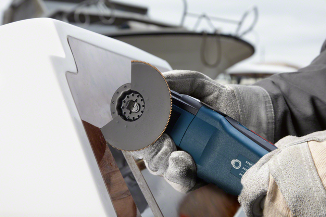 A person wearing safety equipment uses a power tool to cut a glass panel.