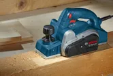 Planer smoothing the surface of a wooden beam on a workbench.