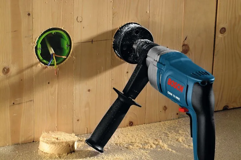 Power drill with a hole saw attachment cutting a circular hole in a wooden wall.