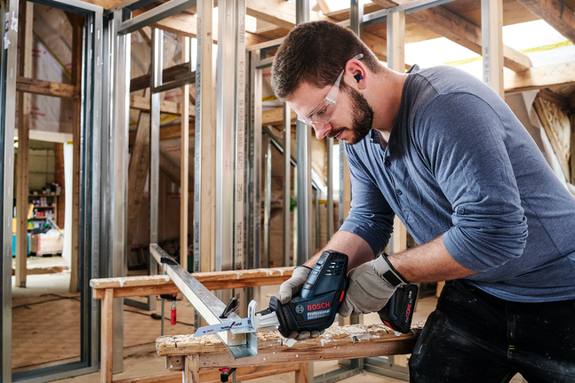 Person wearing safety equipment cuts a metal beam with a power tool indoors.