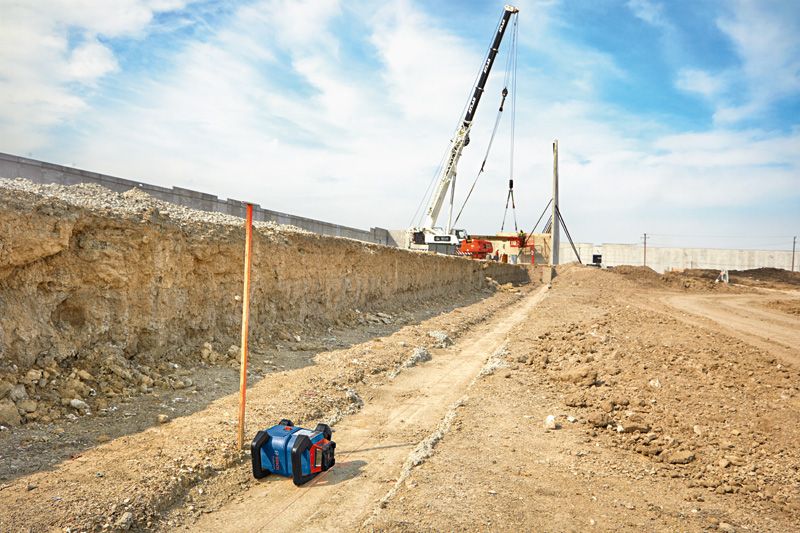 Laser leveling tool set on a construction site with a crane lifting materials in the background.