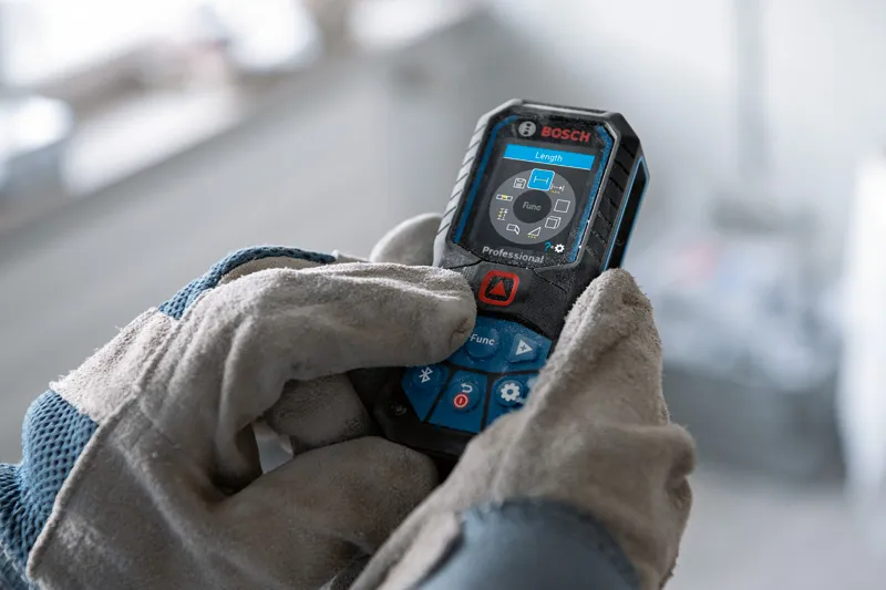 Person wearing safety equipment operates a laser measure with a digital display.