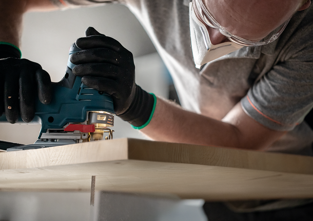 Person wearing safety equipment uses a jigsaw to cut a piece of wood.
