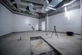 Laser leveling tool on a tripod projects green lines across a tiled room under construction.