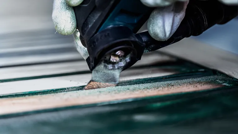 Person wearing safety equipment sanding a wooden surface using a power tool.