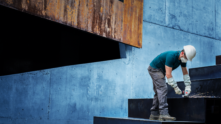 A person wearing safety equipment drills into a metal staircase.