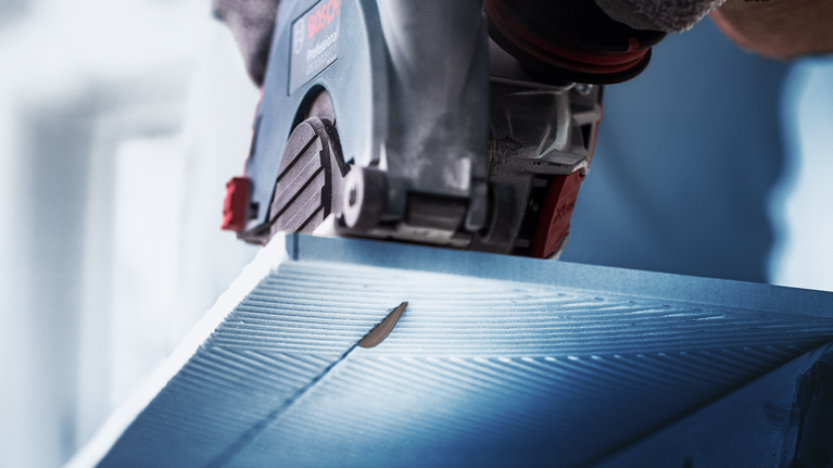 Person wearing safety equipment cuts a blue panel with a circular saw.
