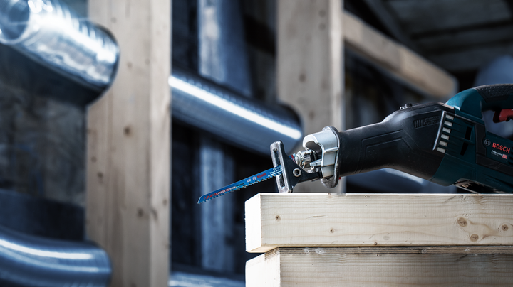 Reciprocating saw cutting through a stack of wooden beams in a construction setting.
