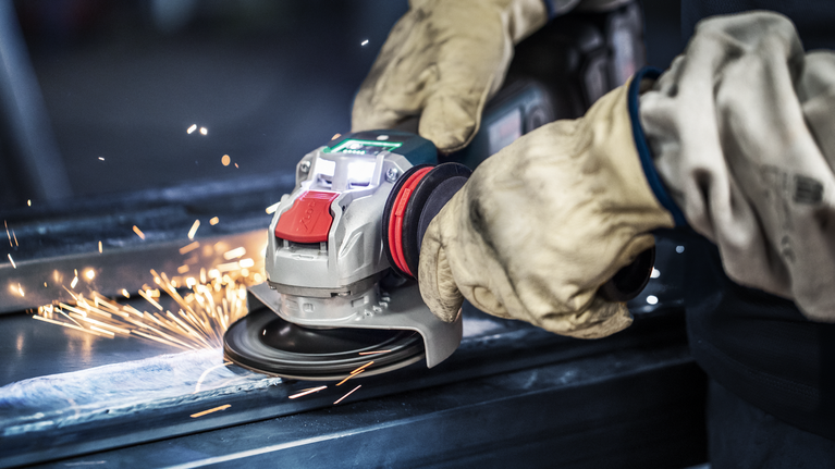 A person wearing safety equipment grinds metal, producing sparks.