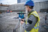 Person wearing safety equipment operates a laser leveling tool at a construction site.