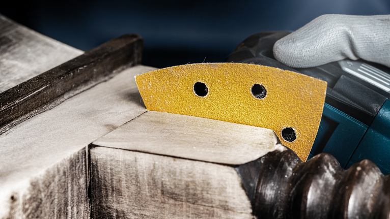 Person wearing safety equipment sands detailed wood molding with a power tool.