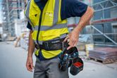 Person wearing safety equipment adjusts a tool belt at a construction site.