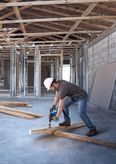 A person wearing safety equipment drills into a wooden beam on a construction site.