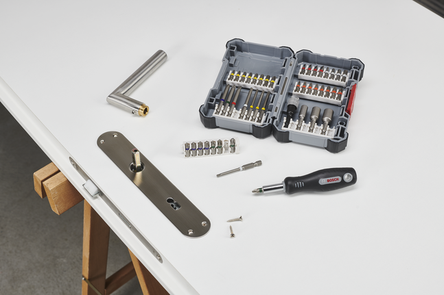 Screwdriver set and metal handle beside a partially installed door lock on a workbench.