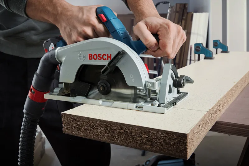 A person uses a cordless circular saw to cut particle board.
