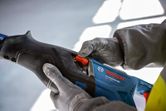Person wearing safety equipment adjusts a power tool with a red switch.