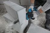 A person wearing safety equipment cuts an AAC block using an electric cutter.