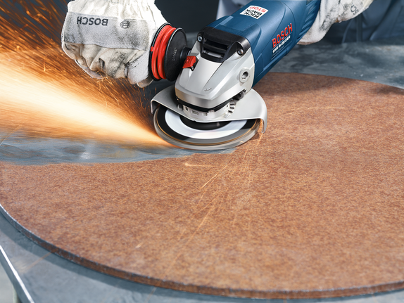 Person wearing safety equipment grinds the edge of a circular sheet, producing sparks.