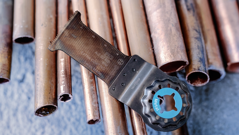 Oscillating multi-tool blade rests on cut copper pipes.