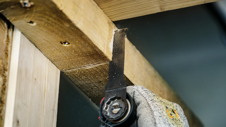 Person wearing safety equipment uses a power saw to cut through a wooden beam.