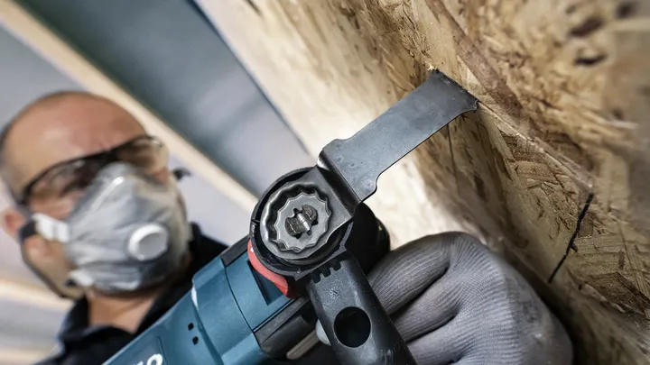 Person wearing safety equipment cutting wood panel with an oscillating multi-tool.