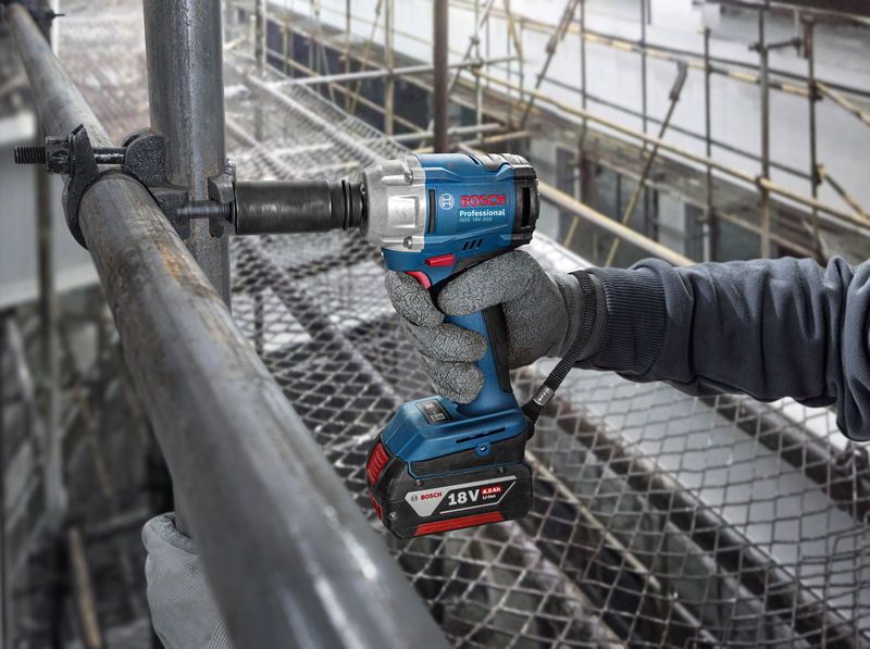 A person wearing safety equipment uses a cordless impact wrench on scaffolding.