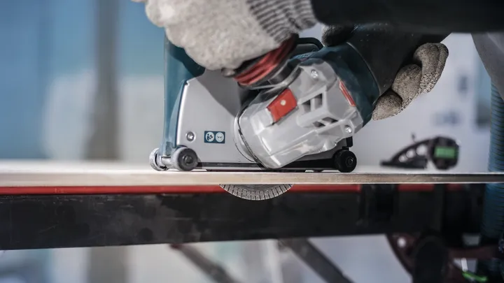 Person wearing safety equipment operates a power tool to cut a tile.