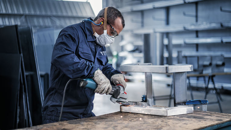 Person wearing safety equipment grinds a metal frame, creating sparks.