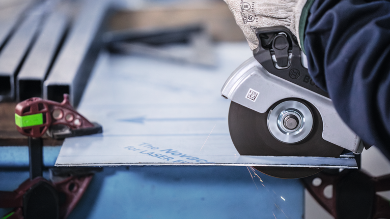 Person wearing safety equipment cuts a metal sheet with a circular saw.