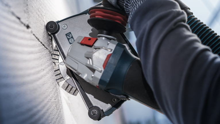 Person wearing safety equipment grinds a wall with a power tool.