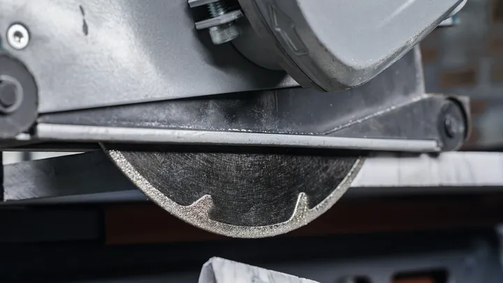 Diamond saw blade cutting a piece of tile in a workshop.