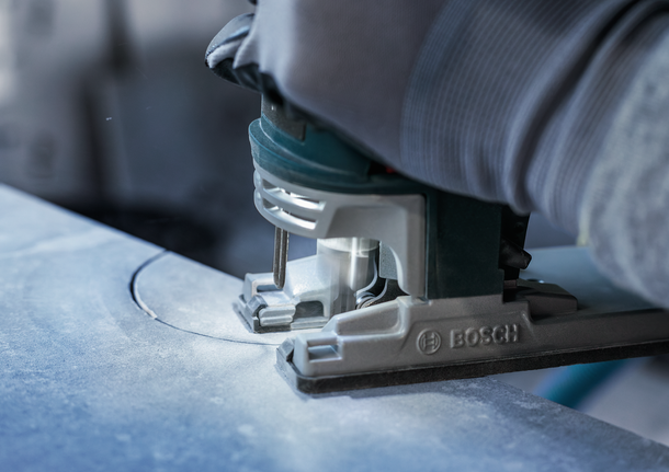 Person wearing safety equipment guides a jigsaw cutting a curved line in stone.