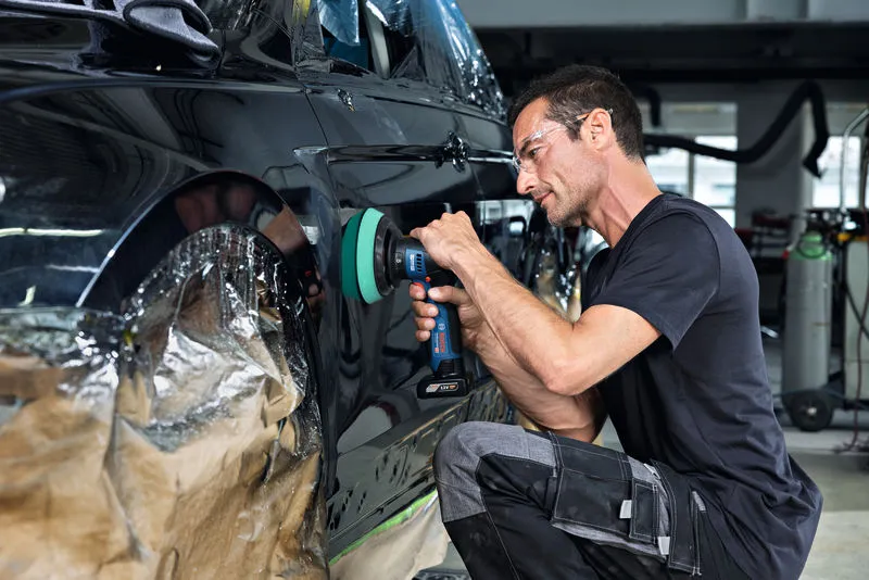Person wearing safety equipment polishes a car door with a cordless polisher.