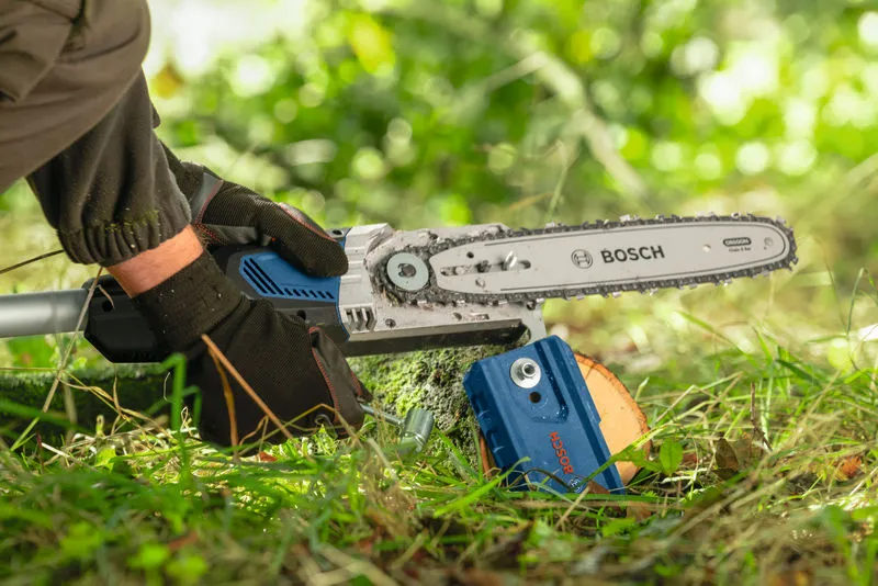 A person wearing safety equipment trims a tree branch using a cordless telescopic pruner.
