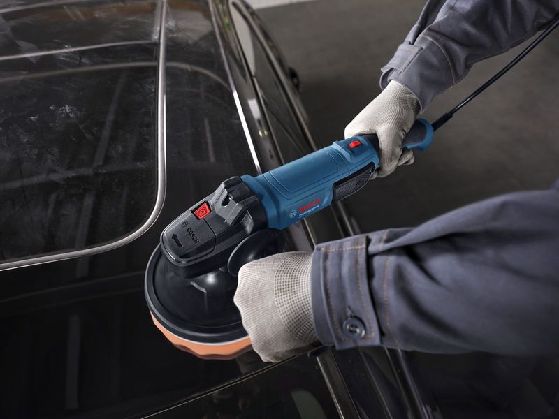 A person wearing safety equipment polishes a car roof with a power polisher.