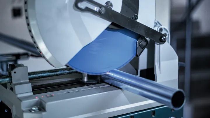 Metal cutting saw slicing a steel pipe in a workshop.