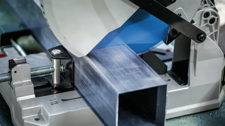 Metal cutting saw slices through a large steel beam in an industrial setting.