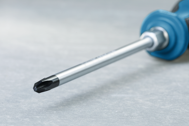 Phillips screwdriver with a blue handle resting on a grey surface.