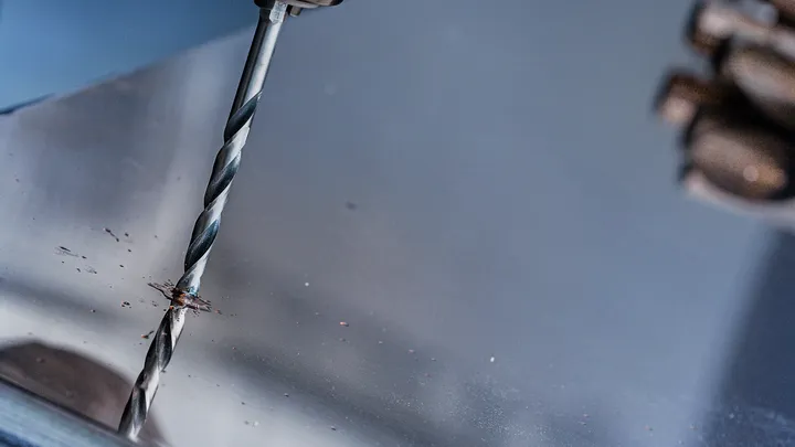 Person drills into a metal sheet.