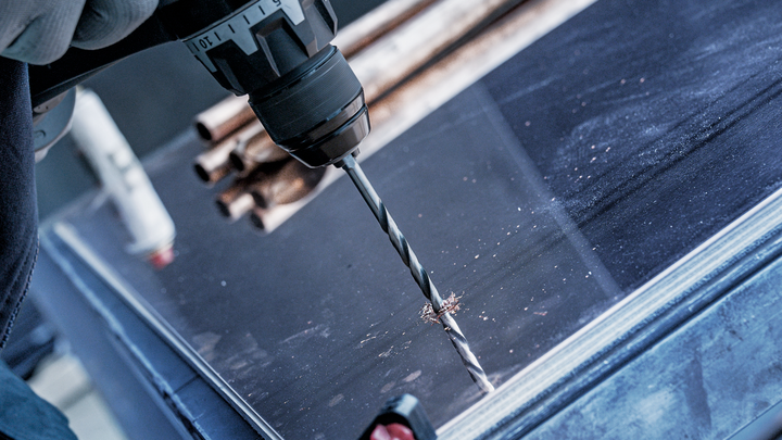 Person using a power drill to make a hole in a metal sheet.