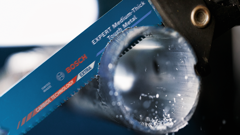 Saw blade cutting through a metal pipe with metal shavings visible.