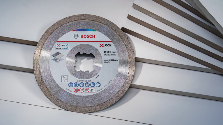 Diamond cutting disc positioned next to multiple tile edges on a white surface.