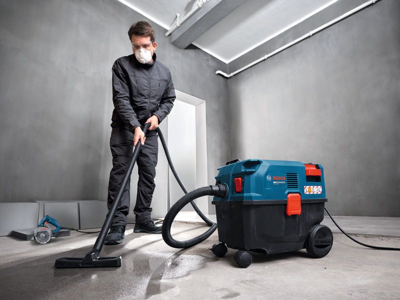 A person wearing safety equipment uses an all-purpose extractor to clean a concrete floor.