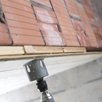 منشار ثقب يحفر من خلال الخشب أسفل صف من الطوب المكدس.