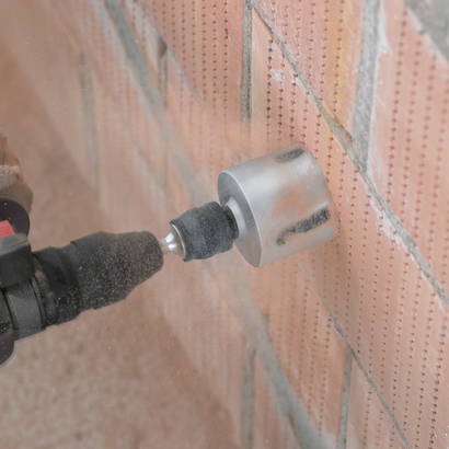 مثقاب دوار مزود بملحق منشار ثقب يقطع جدارًا من الطوب.