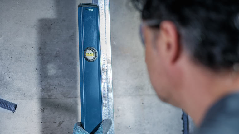 يقوم شخص يرتدي معدات السلامة بفحص المحاذاة باستخدام ميزان تسوية مقابل عارضة معدنية.